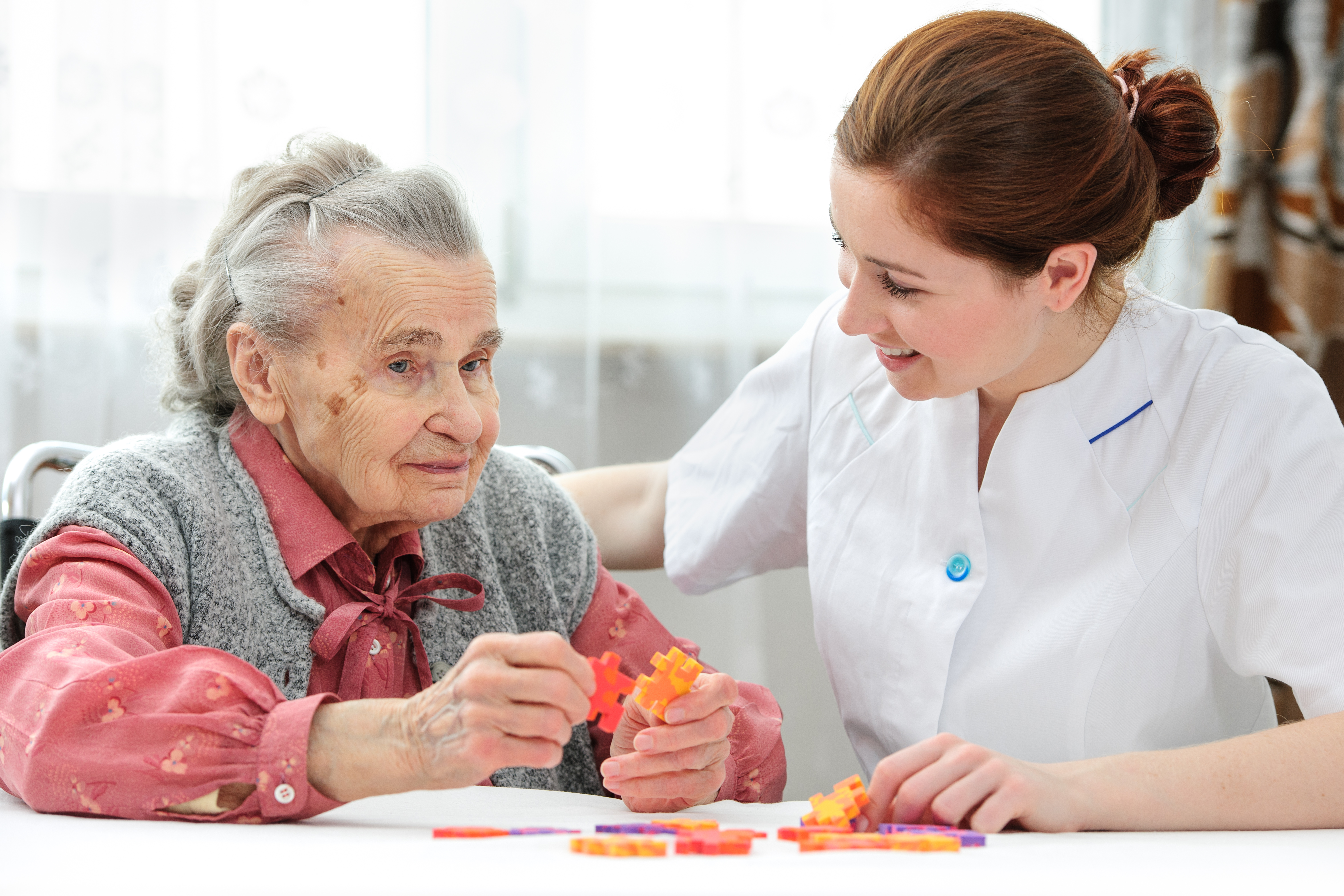 Nurse helps the senior woman jigsaw puzzle to solve in a nursing home
