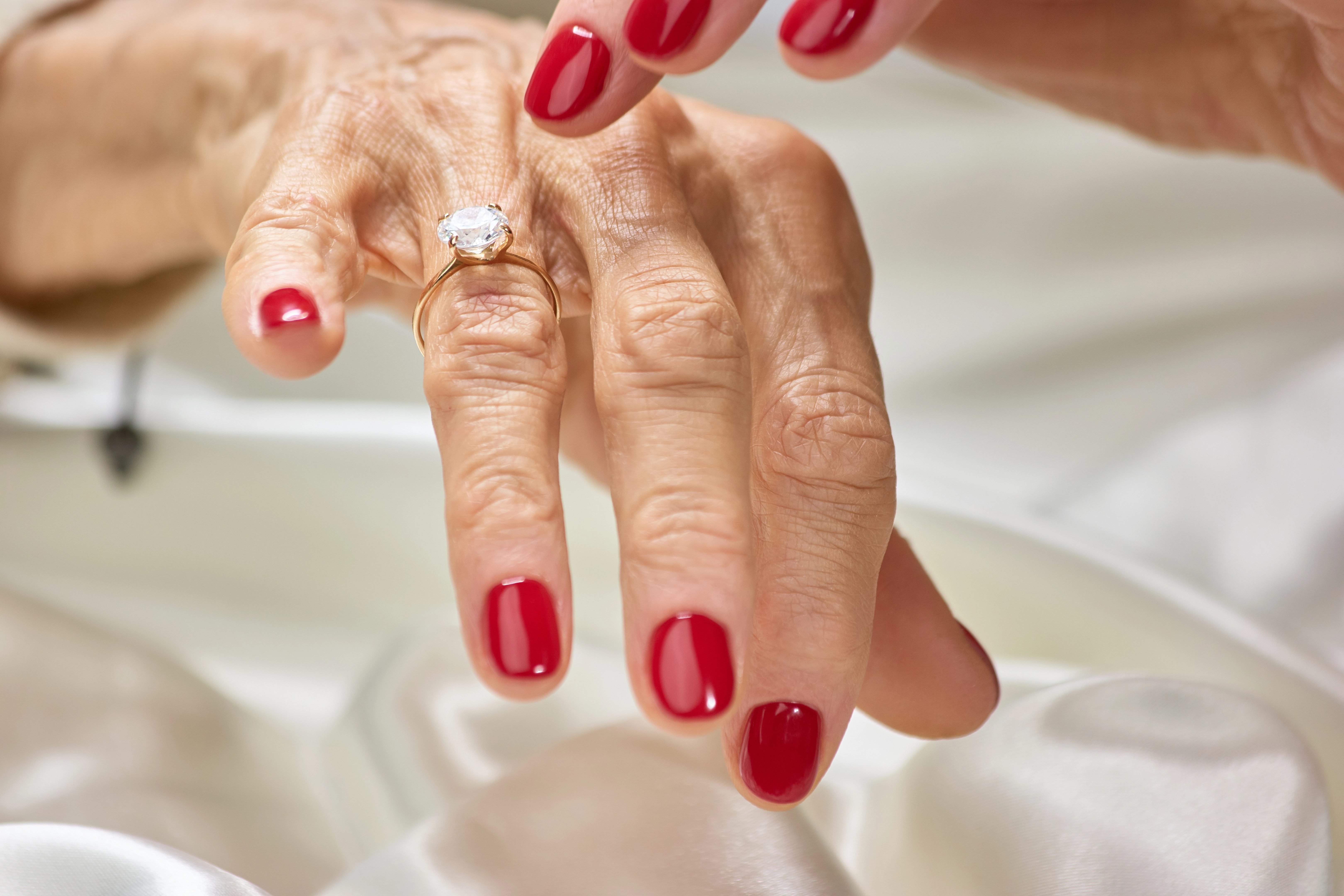 Female finger indicating on diamond. Senior woman with red nails showing her golden ring with precious jewels.