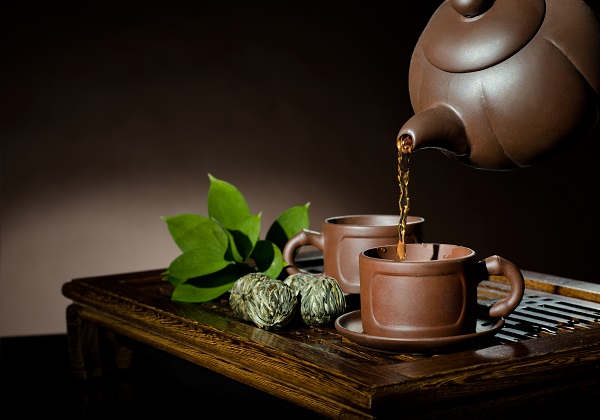 horizontal photo, of the clay teapot tea flow in  cup on brown background,  tea ceremony