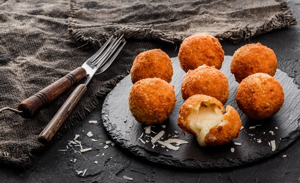 Fried potato cheese balls or croquettes with spices on black plate over dark stone background. Unhealthy food, top view