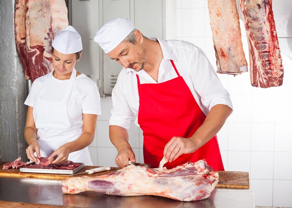 Mature male and female butchers working at counter in shop