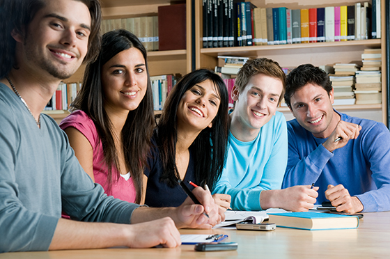 Happy group of young students studying together in a college library and looking at camera smiling