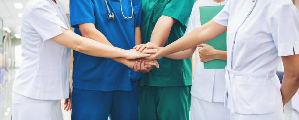 Cooperation of people in the medical community teamwork with a hands together between the doctor in the green, blue uniform and nurses in white dress at hospital. Fight covid 19 virus healthy concept.