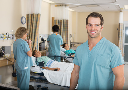 Portrait of young male nurse with colleagues examining patients in PACU